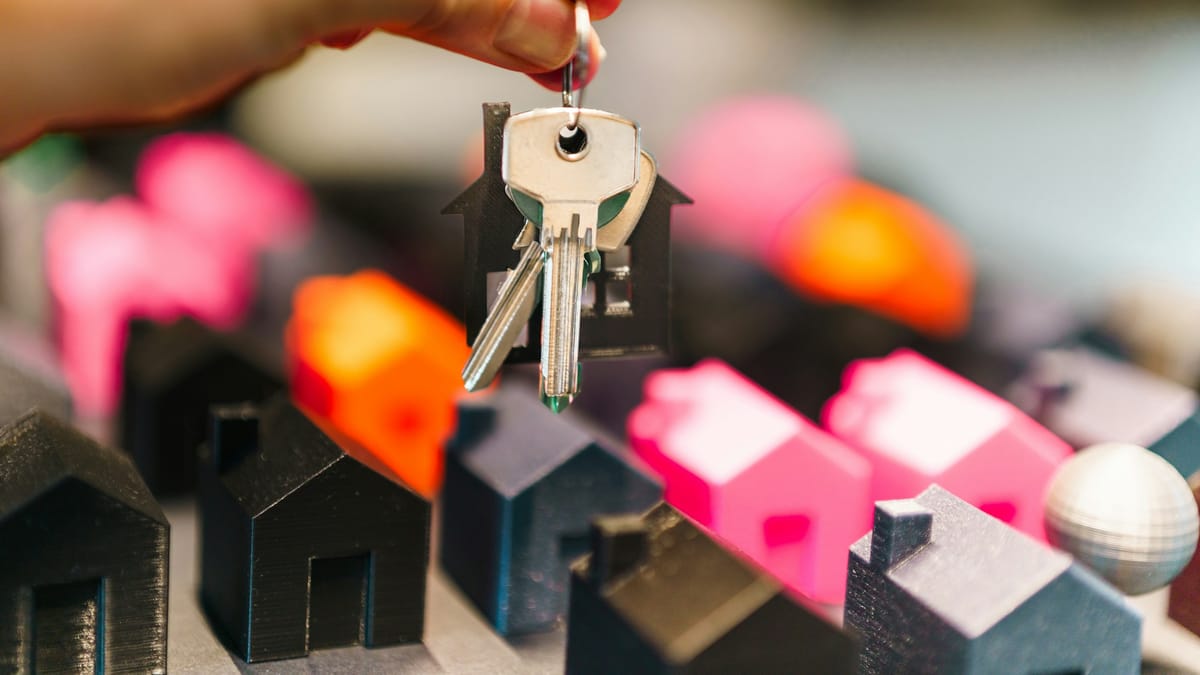 A hand holding house keys above a row of miniature houses