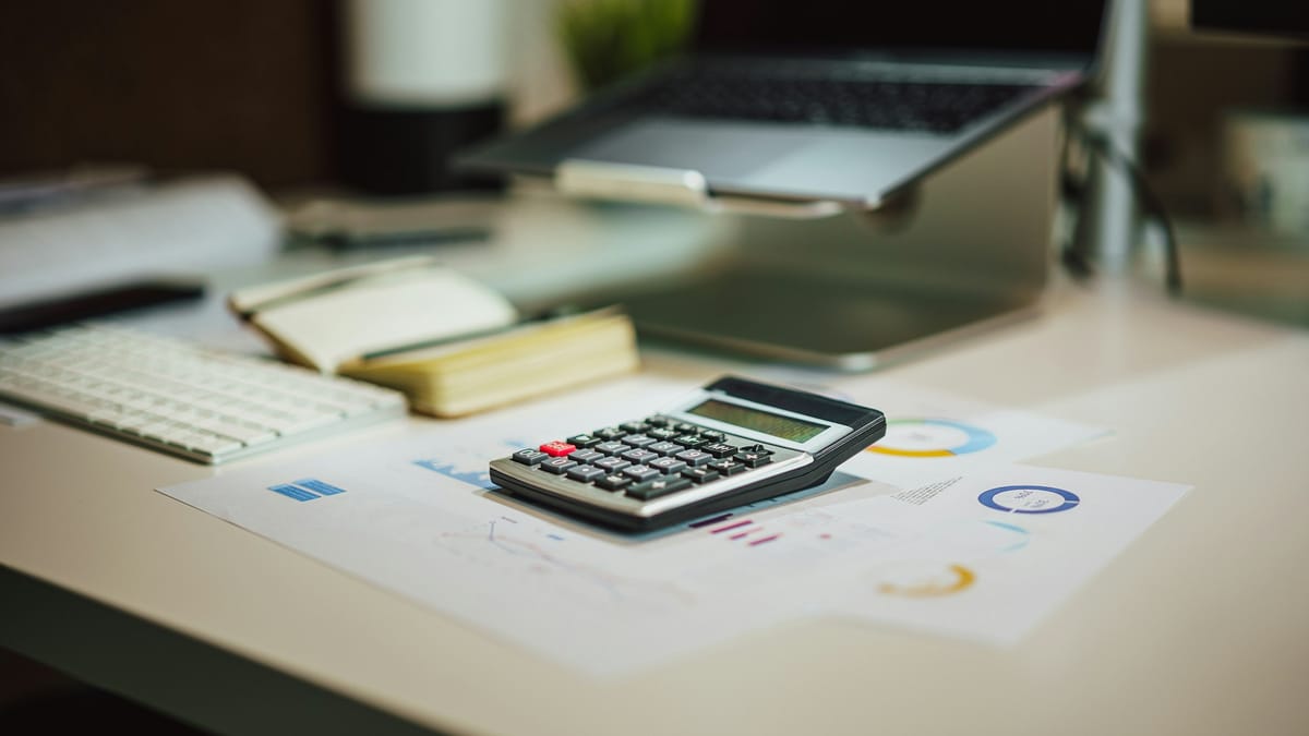 A calculator and notebook on a desk beside a laptop, used to work out take-home pay